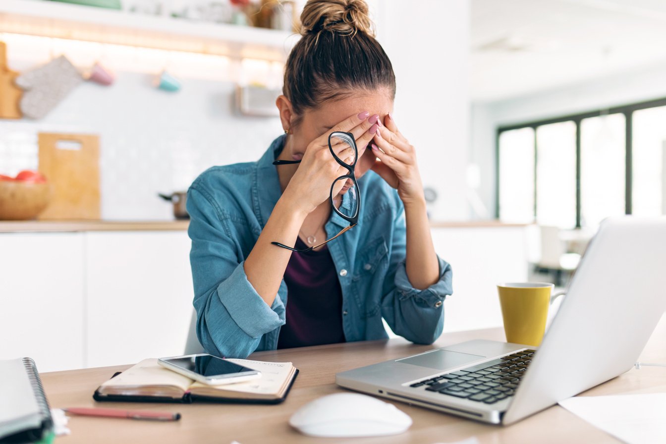 Stressed business woman working from home on laptop looking worried, tired and overwhelmed int he kitchen at home.