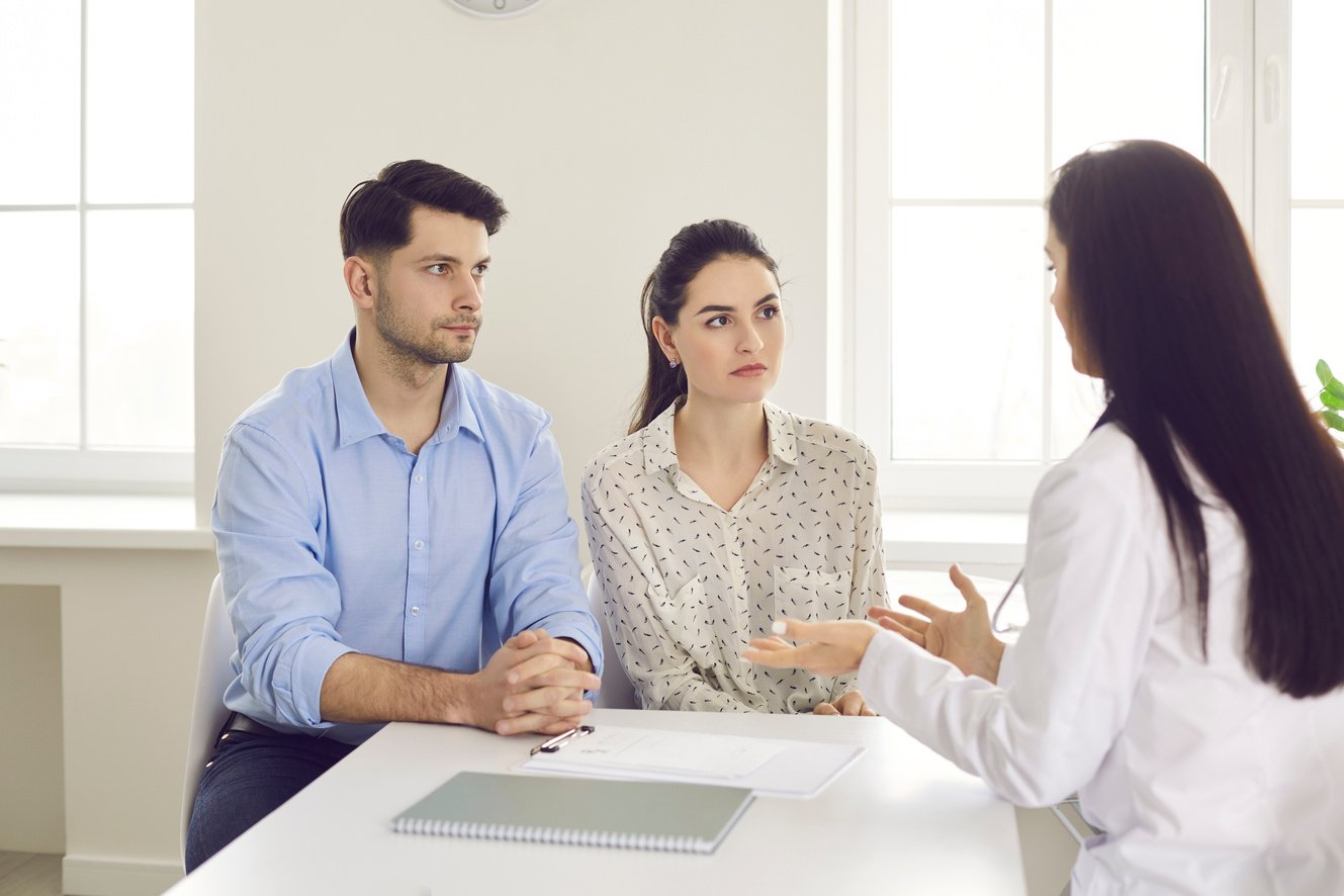 Doctor Counseling Millennial Family Couple about Medical Treatment at Clinic