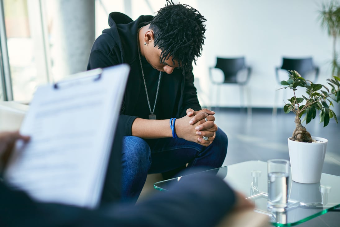 Depressed black teenage boy having counselling with mental health professional.